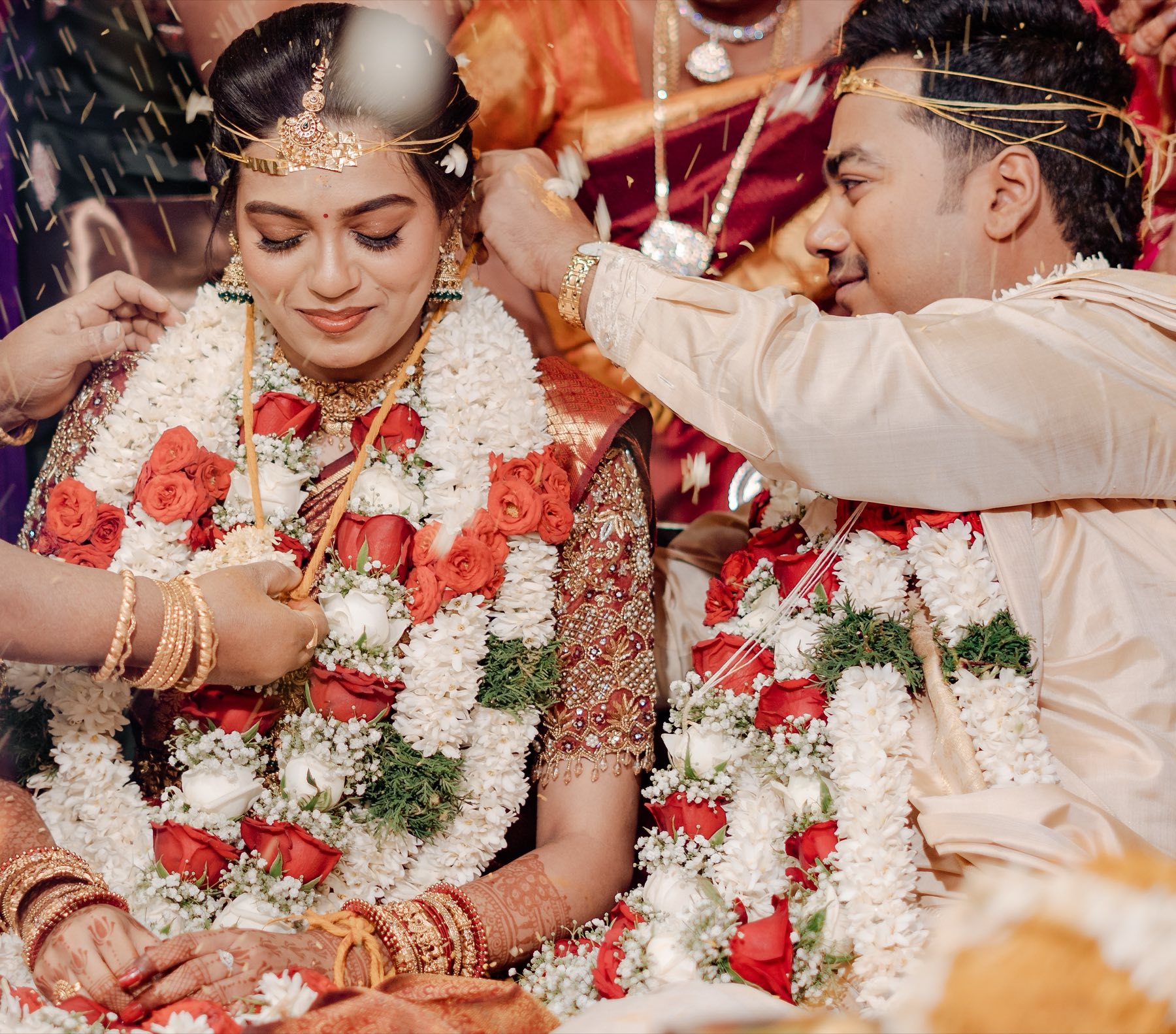Family showering blessings and petals as the couple exchange garlands